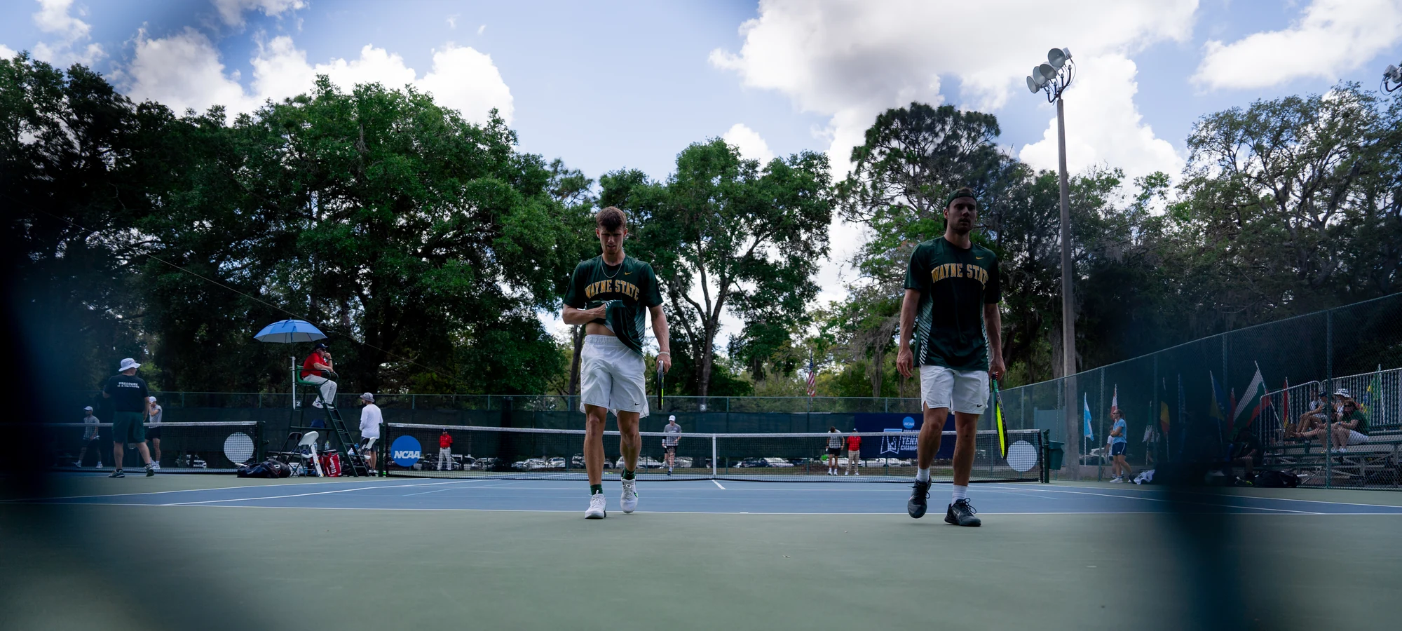 Two Wayne State University tennis players walking towards the camera across a hard court.