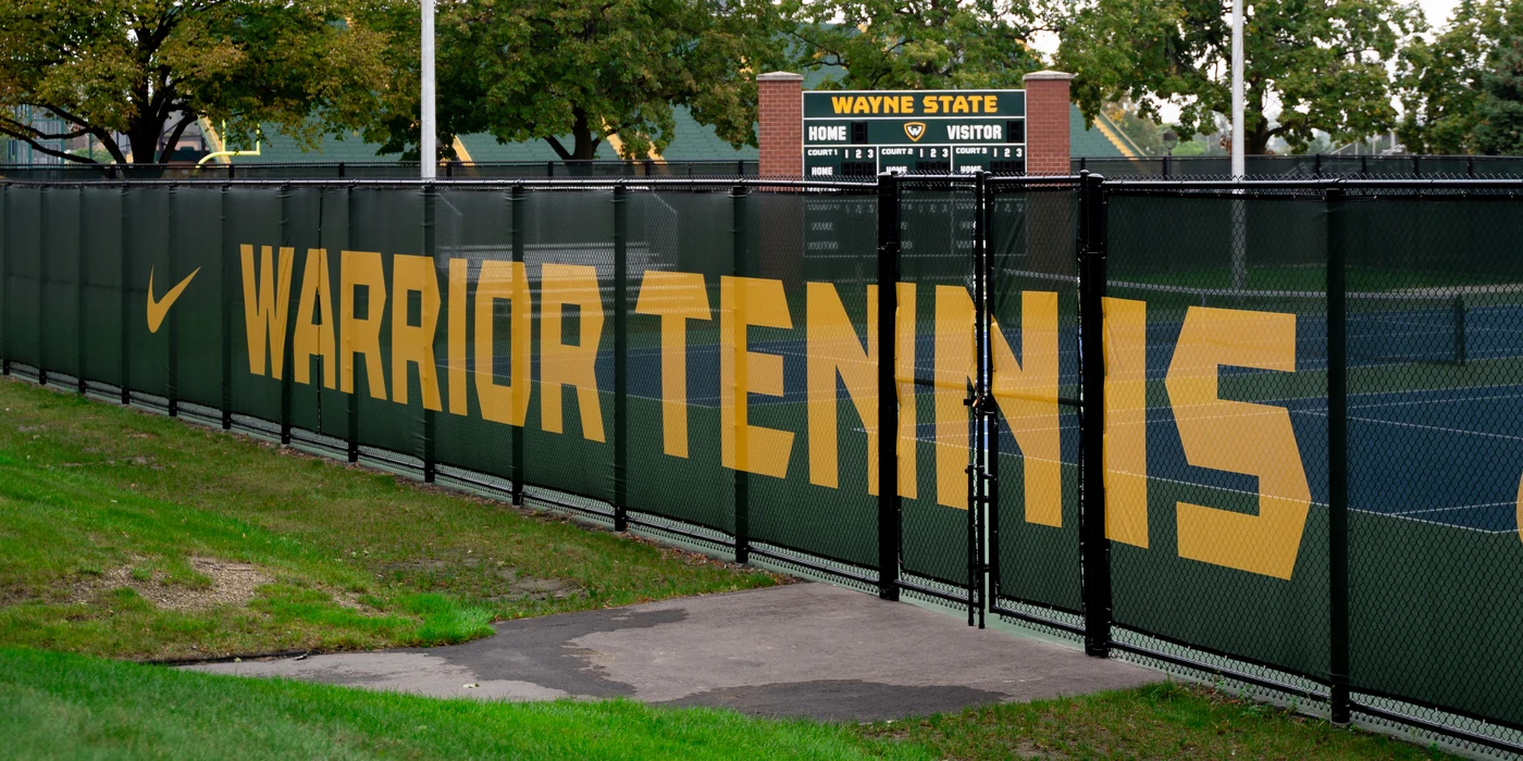 The gold Warrior Tennis banner along the courtside fence where 313 Tennis coaches.